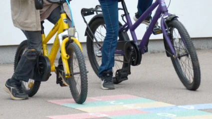 Två barn som cyklar på en skolgård med en färgglad hopphage.
