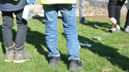 Barn står i grupp och tittar på olika avfallstyper på en grön gräsmatta.