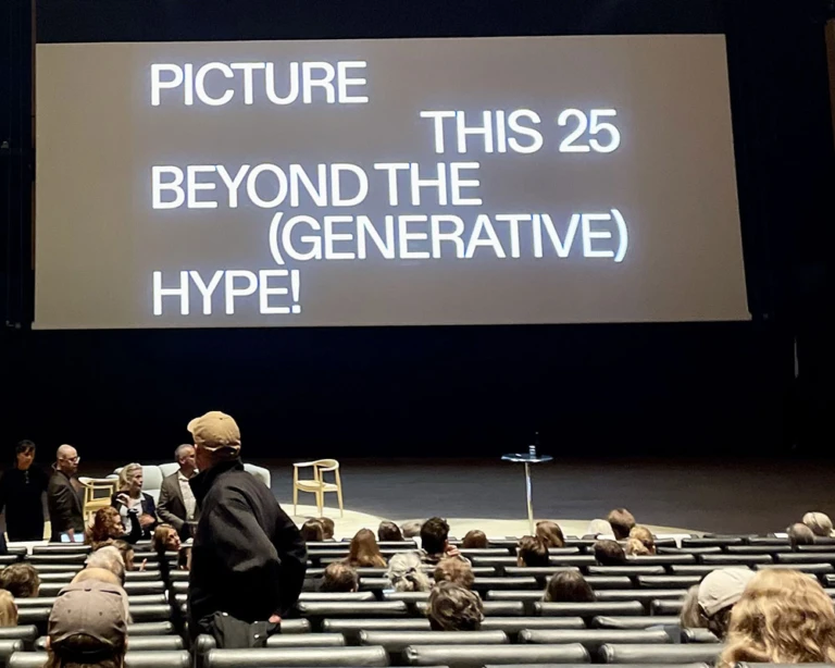 Konferenssal där publik anländer på skärmen står det "Picture this 25 Beyond The (Generative) Hype"