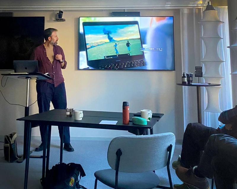 En person föreläser i en lektionssal och visar film på en bildskärm.