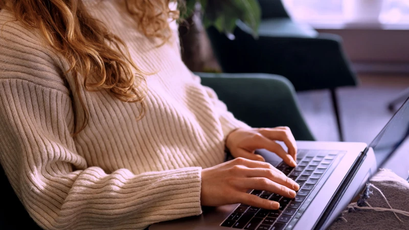 Kvinna med laptop i knät och händerna skriver.