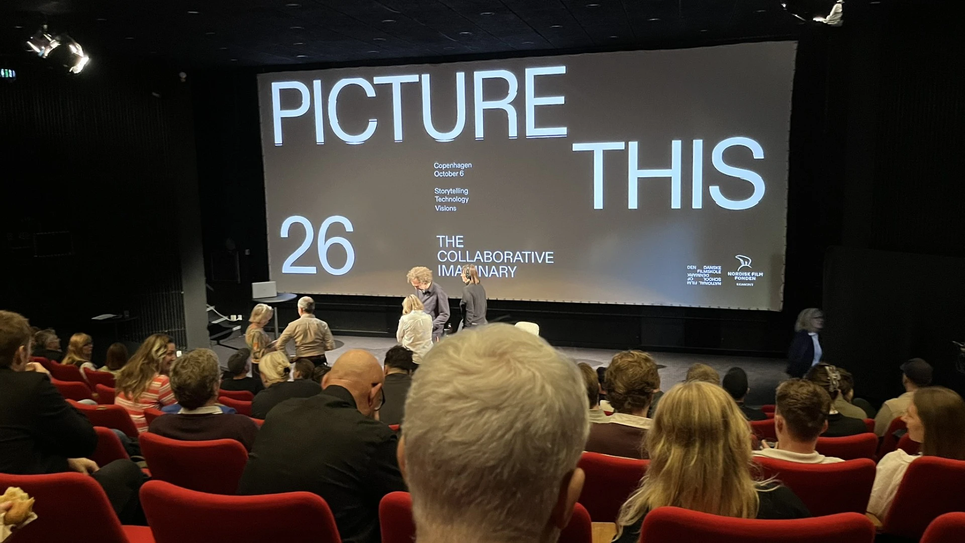 Publik samlas i konferenssal och på väggen står det Picture this 26