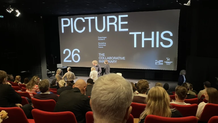 Publik samlas i konferenssal och på väggen står det Picture this 26